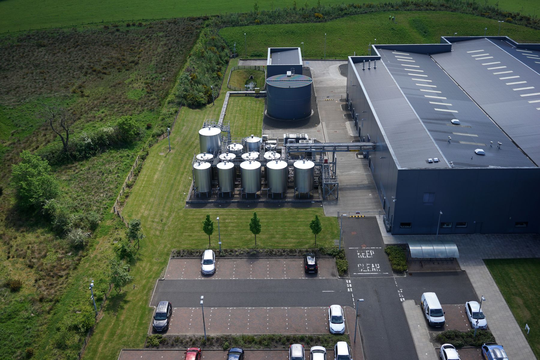 Oblique aerial photo of a drinks production plant, with the fragile roof, bunded tank farm, bulk storage tank, pipe bridge, service yard, emergency access, pedestrian routes and fire assembly point marked