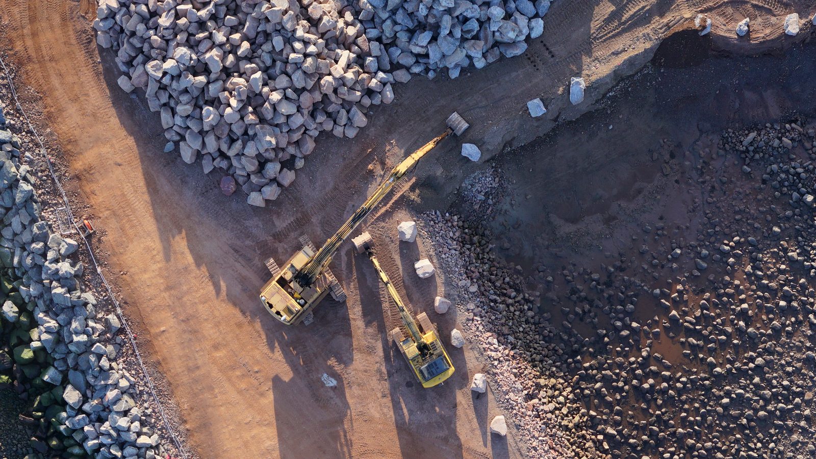 Straight-down drone photo of two excavators placing rock on a harbour breakwater